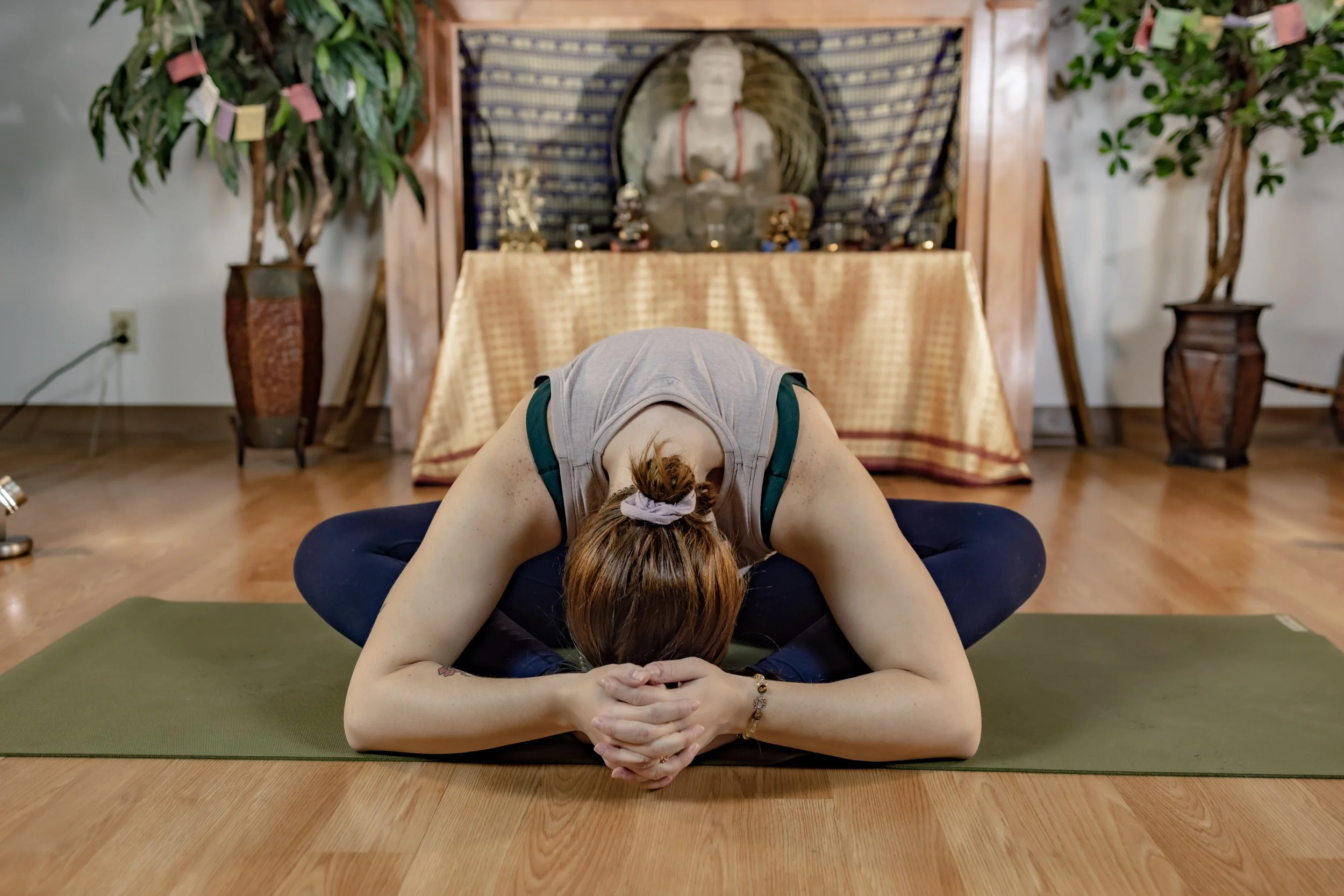 Sydney folded forward in yoga pose in front of Buddha statue on an alter